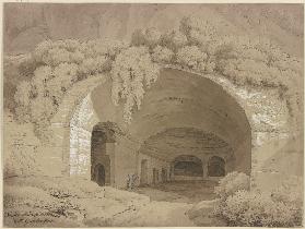 Blick in ein antikes Gewölbe an einem Berghang, von Buschwerk umrahmt, in der Grotte zwei Figuren
